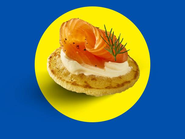 Smoked salmon blini with cream cheese and dill on a yellow circle background.