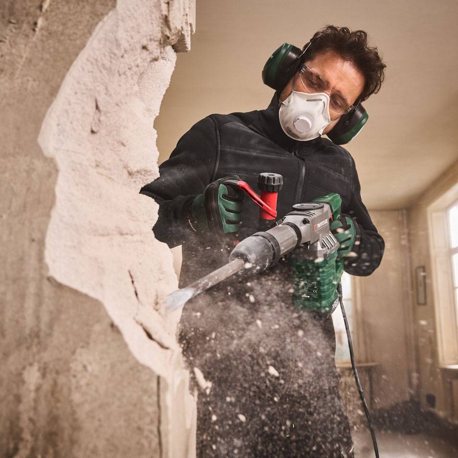 Man with demolition hammer and protective gear demolishing a wall.
