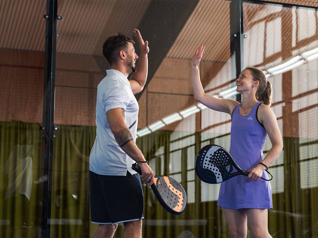 Two padel players, a man and a woman, high-fiving on the court.