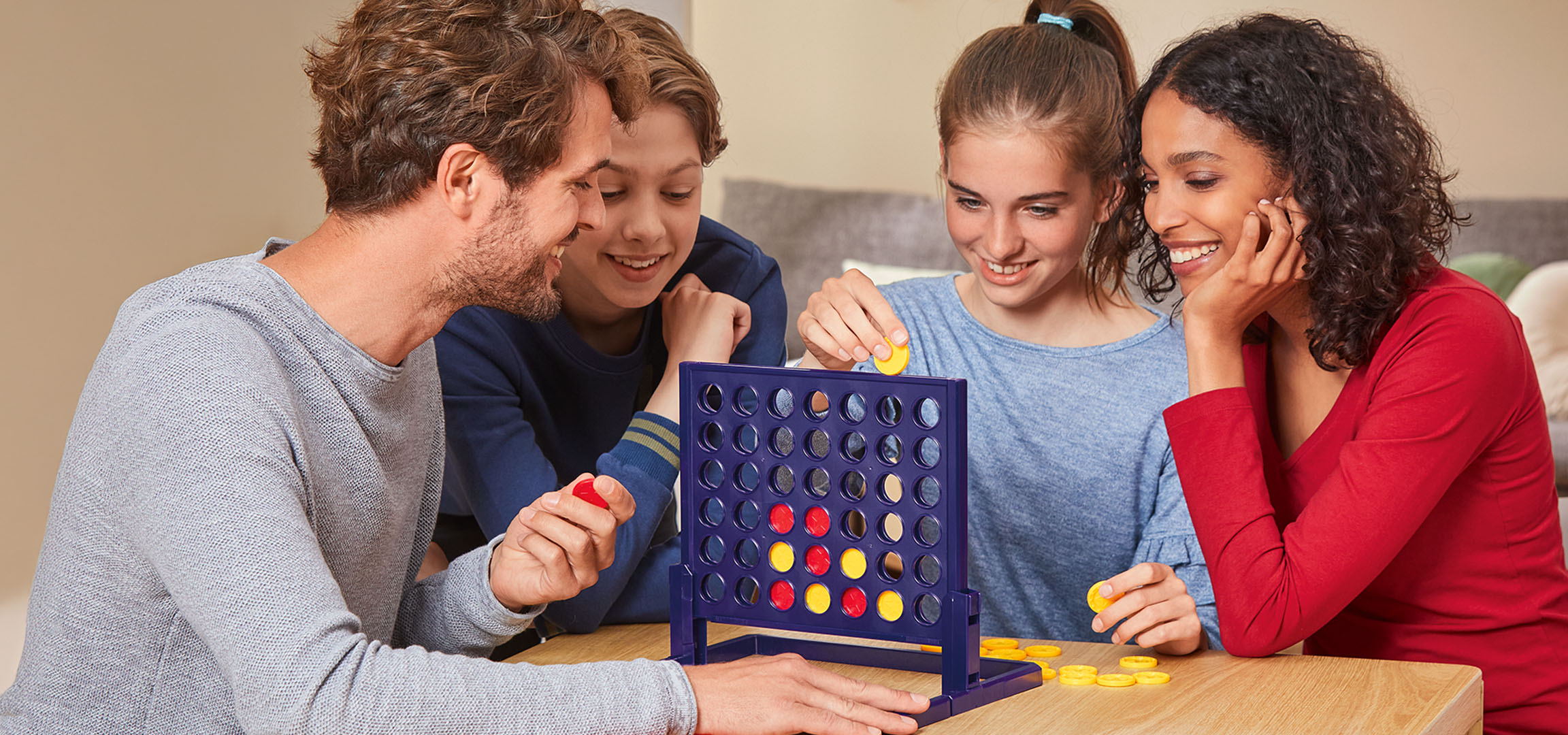 Four people playing the Connect 4 board game at a wooden table.