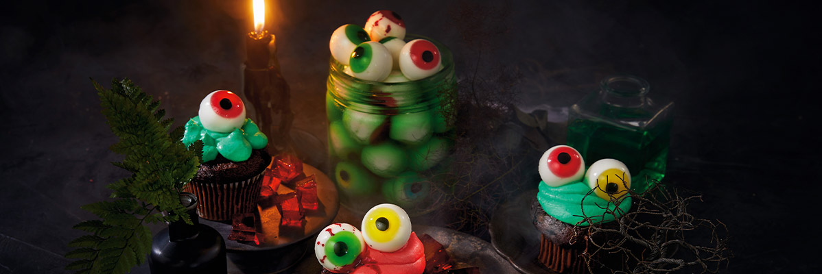 Halloween cupcakes and candies with eyeball decorations, a candle, and a green potion bottle.