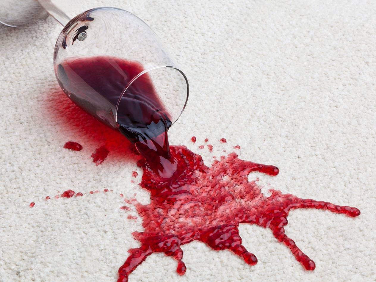 Red wine spilled from a glass onto a white carpet