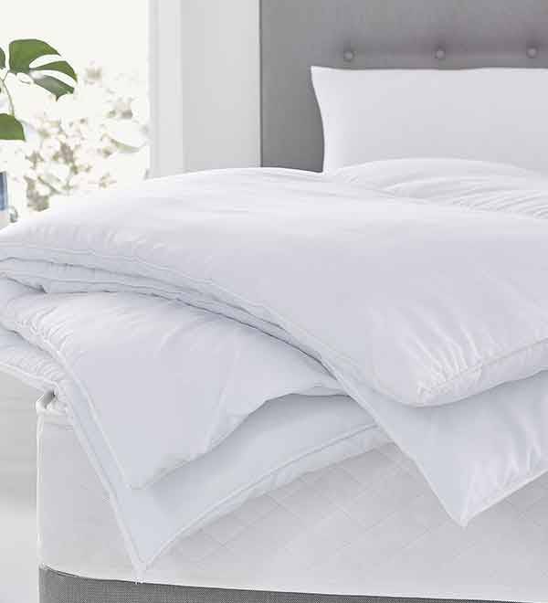 White duvet and pillows on a bed with a grey headboard.
