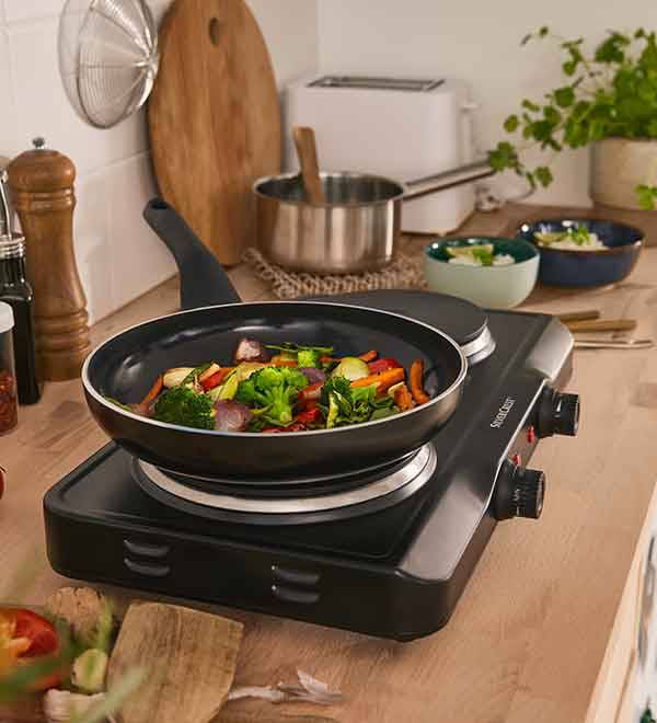 A black SilverCrest hot plate with a pan of stir-fried vegetables on a kitchen counter.