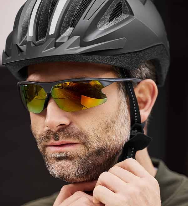 A man wearing a black cycling helmet and yellow-tinted sports sunglasses adjusts his gear.