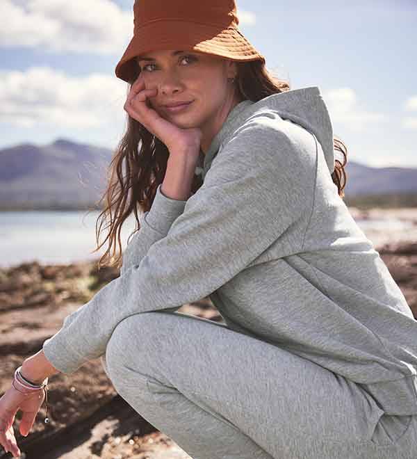 A woman wearing a grey hoodie and orange bucket hat sits outdoors.