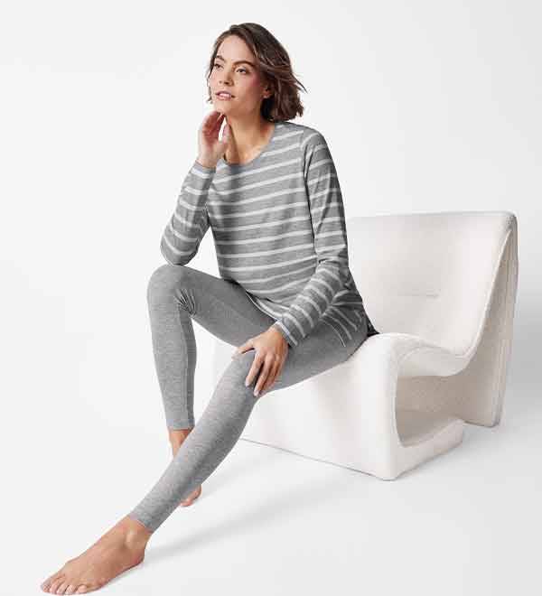 Woman in grey striped long-sleeve shirt and leggings sitting on a white chair.