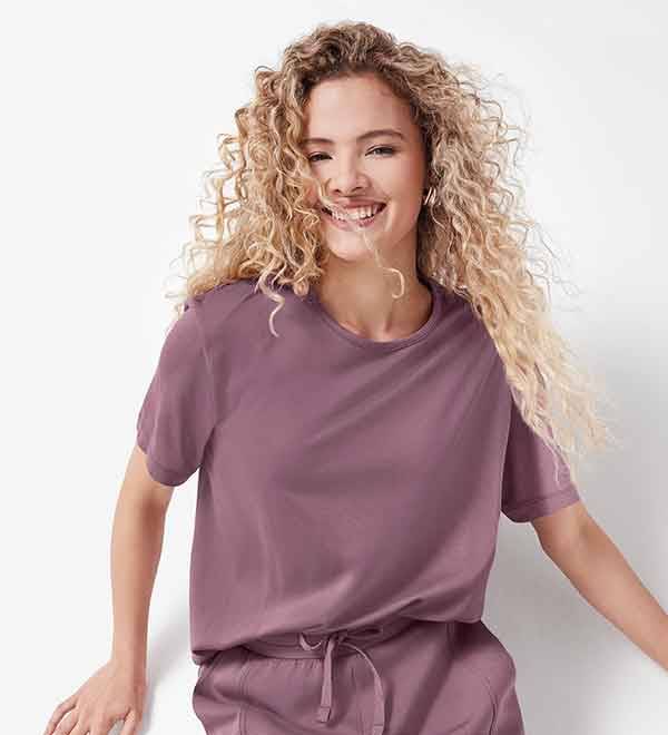 A woman smiles while wearing a mauve short-sleeved t-shirt and matching shorts.