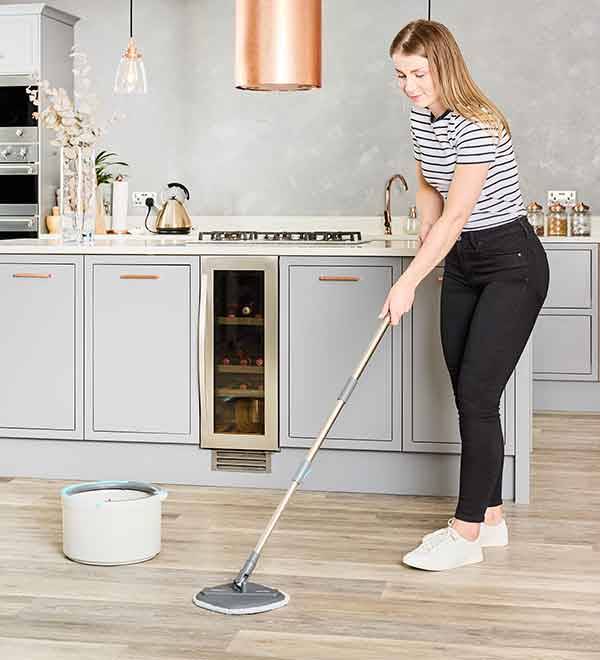 A woman mops a kitchen floor with a spin mop and bucket system.