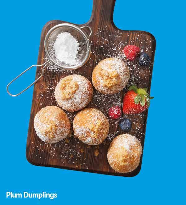 Plum dumplings dusted with powdered sugar, served with fresh berries on a wooden board.