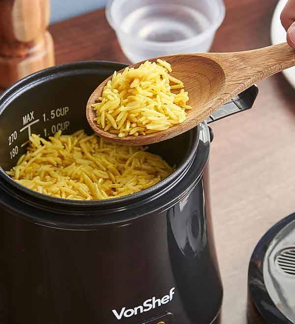A Vonshef rice cooker filled with orzo pasta, with a wooden spoon holding more orzo.