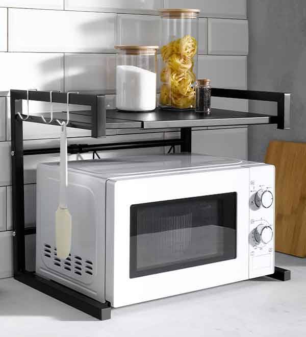 A black microwave oven stand with two shelves holds a microwave, pasta, sugar, and spices.