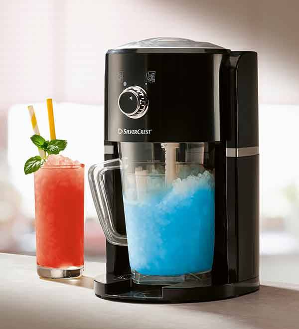 A SilverCrest slush maker creates a vibrant blue slushy drink next to a glass of red juice.