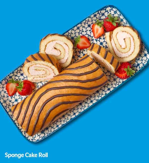 Sponge cake roll decorated with chocolate stripes, served with strawberries on a patterned plate.