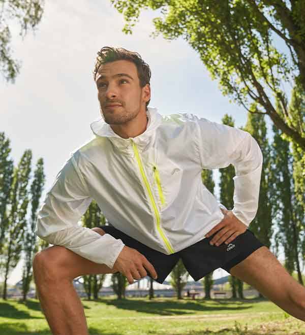 A man in a white jacket and black shorts stretching outdoors.