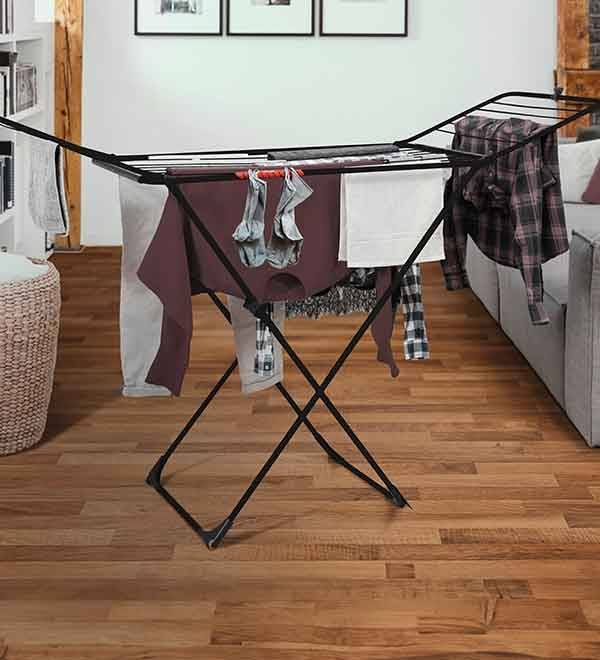 A black metal clothes drying rack holds various garments in a room with hardwood floors.