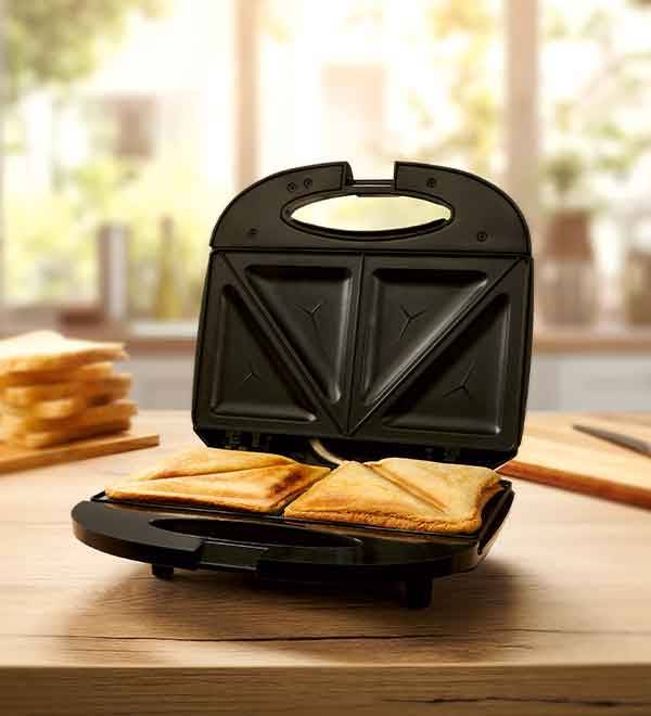 A black sandwich maker sits on a wooden table with toasted sandwiches inside.