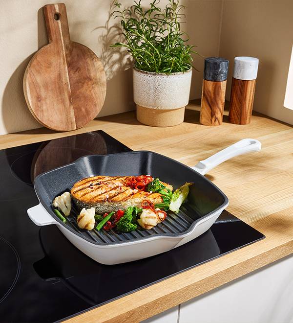 A grilled salmon and vegetables in a grill pan on an induction cooktop.