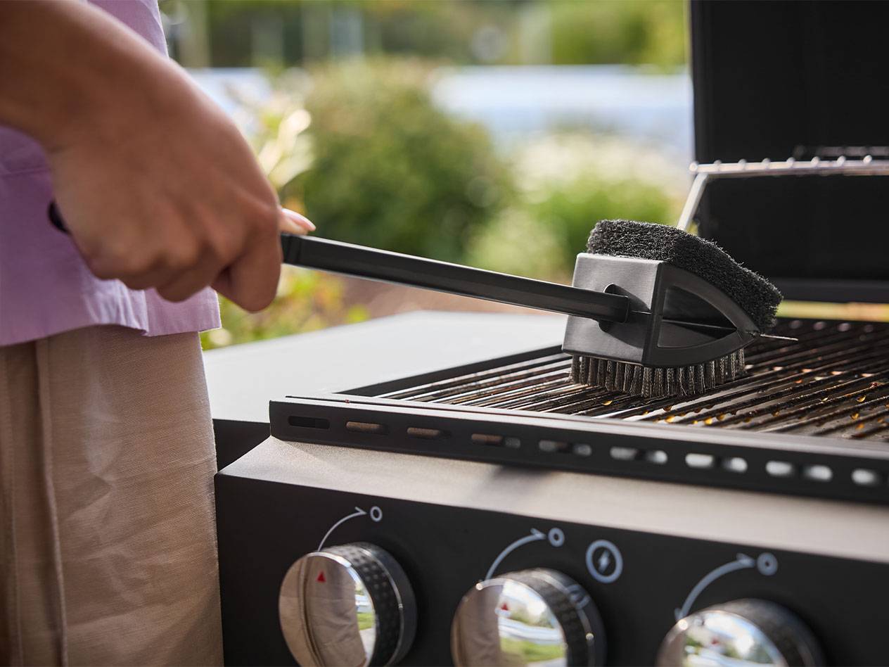 Person cleaning a barbecue grill with a long-handled brush.