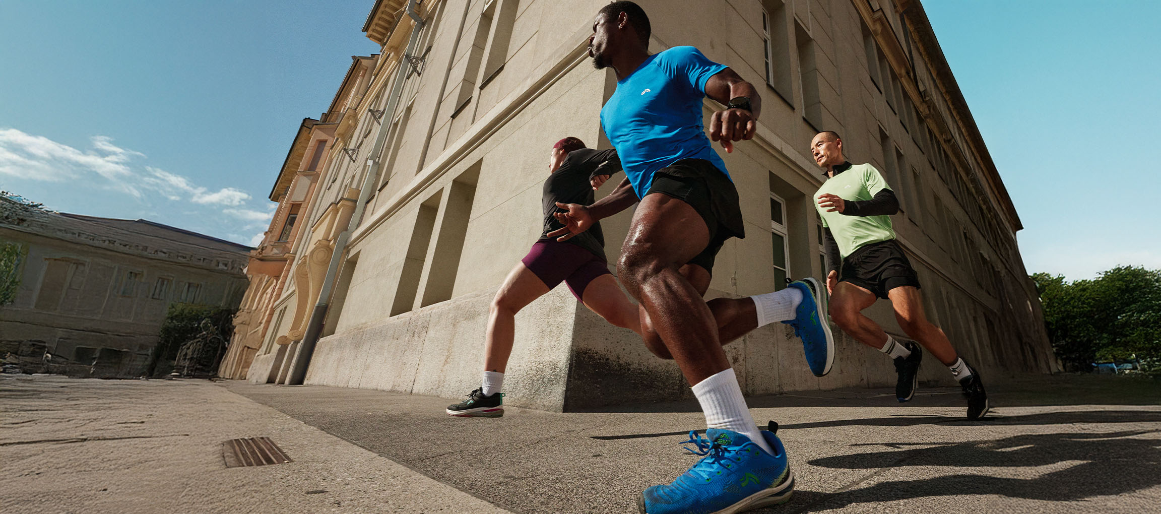 Three runners in sportswear running down a city street.