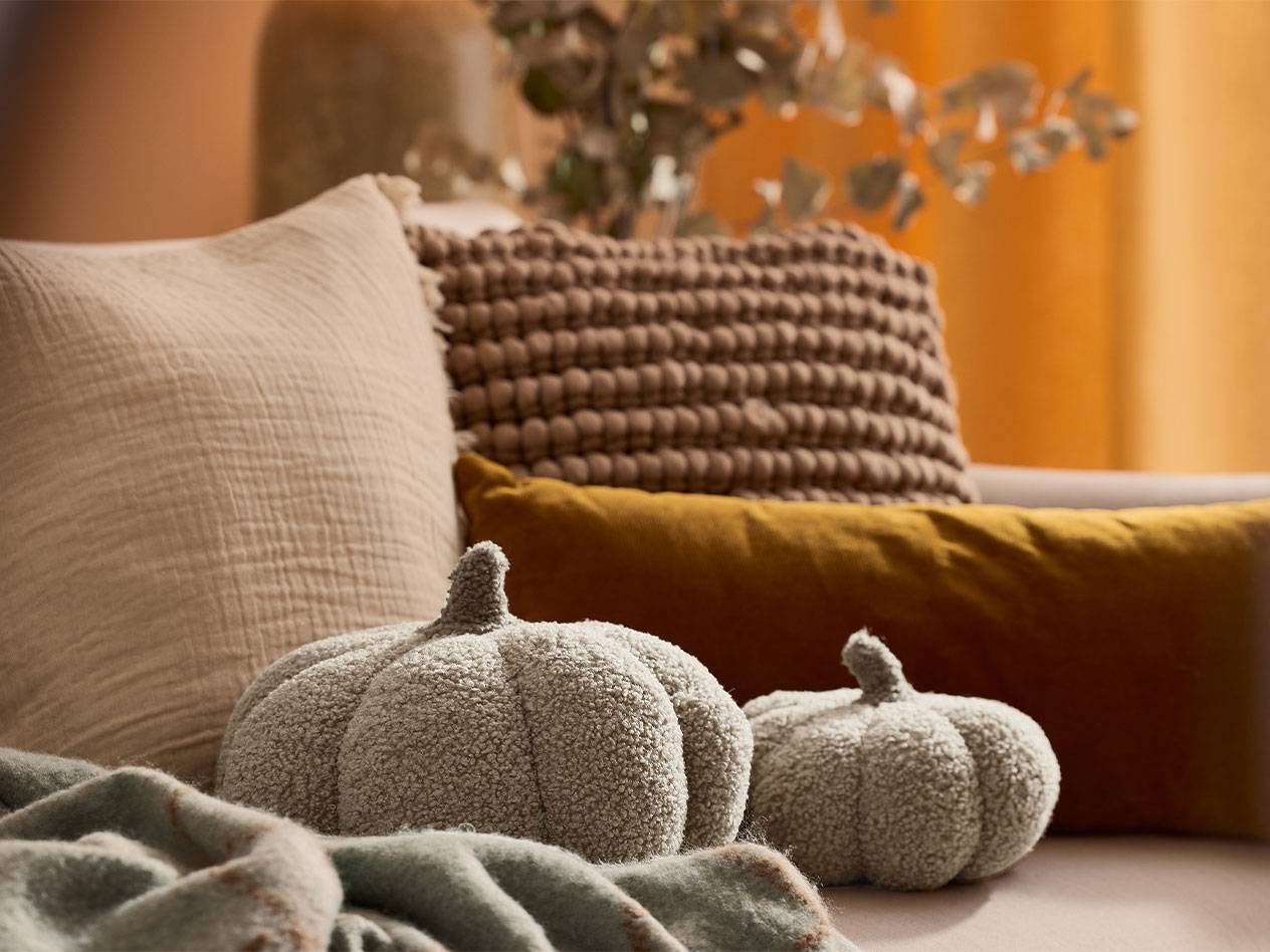 Two plush decorative pumpkins and pillows in earthy tones on a sofa.