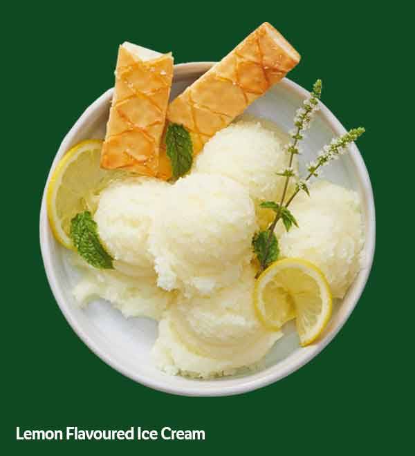 Lemon-flavored ice cream scoops with lemon slices, mint, and wafer rolls in a white bowl.