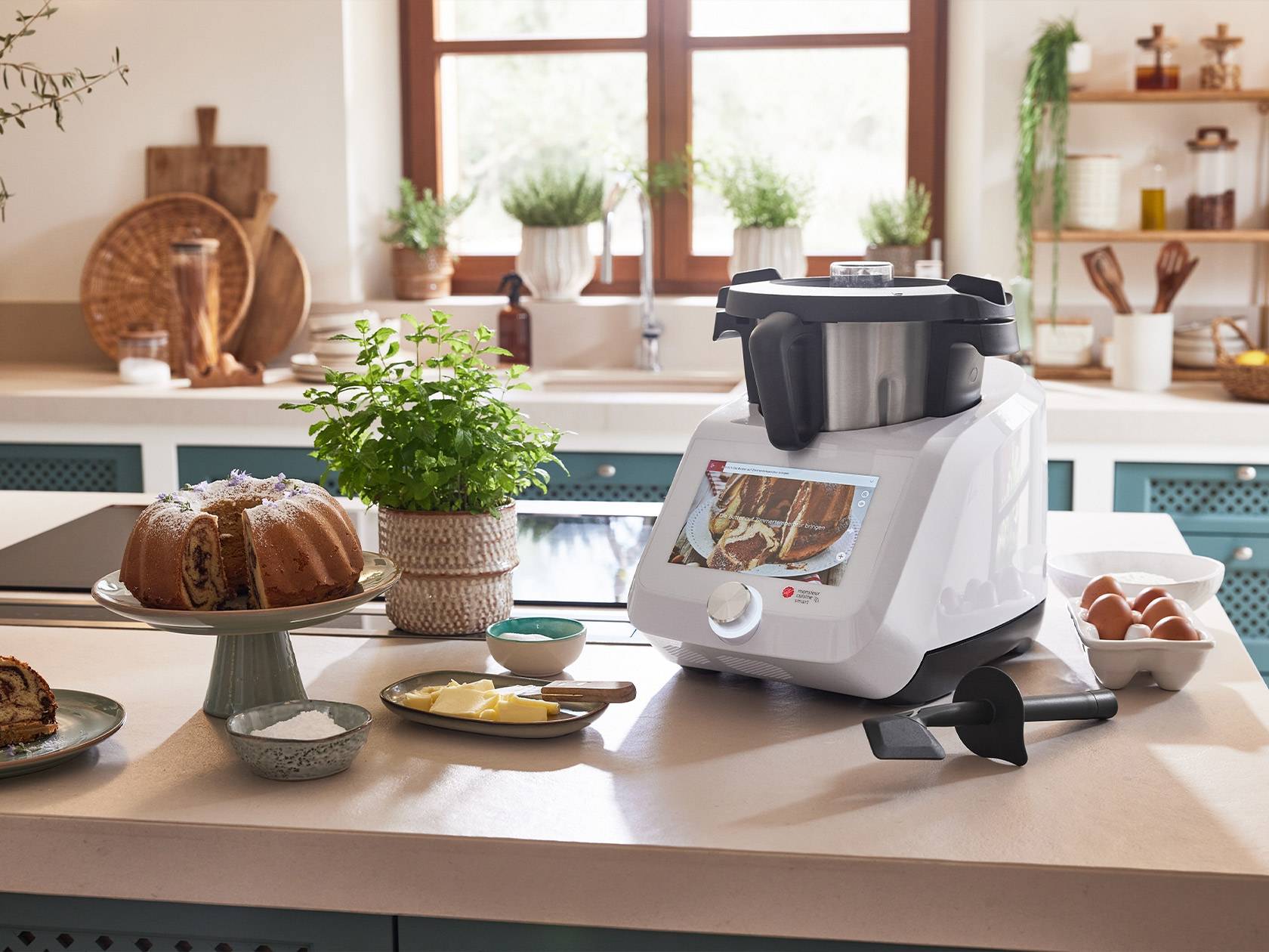 A kitchen counter with a white food processor, a bundt cake, and baking ingredients.