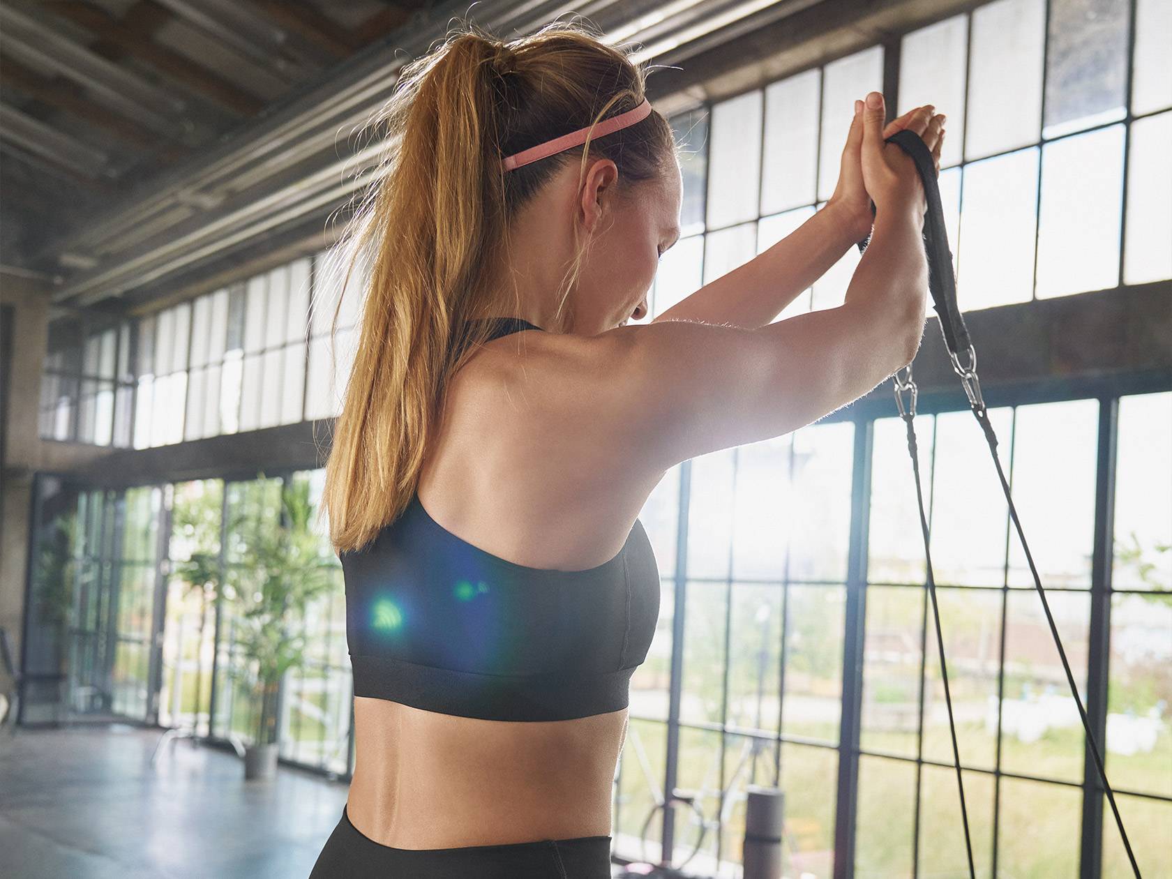 Woman in a sports bra exercising with resistance bands in a gym.