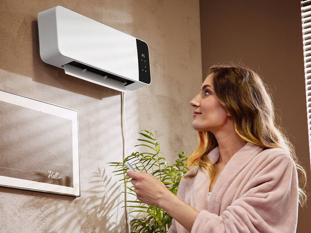 Woman in bathrobe adjusts wall-mounted air conditioner with remote control.