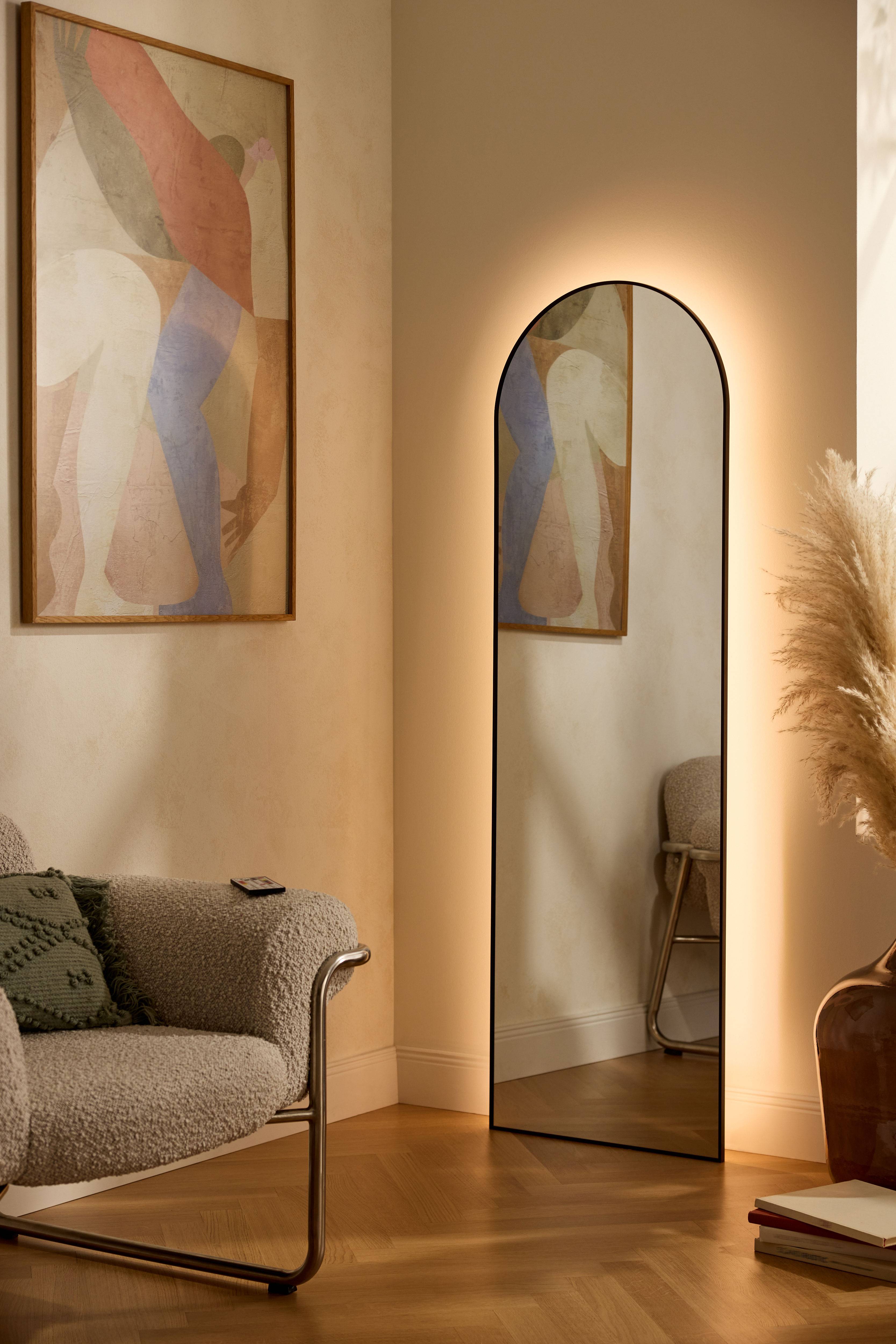 Illuminated mirror and abstract painting in a modern living room with an armchair and pampas grass.