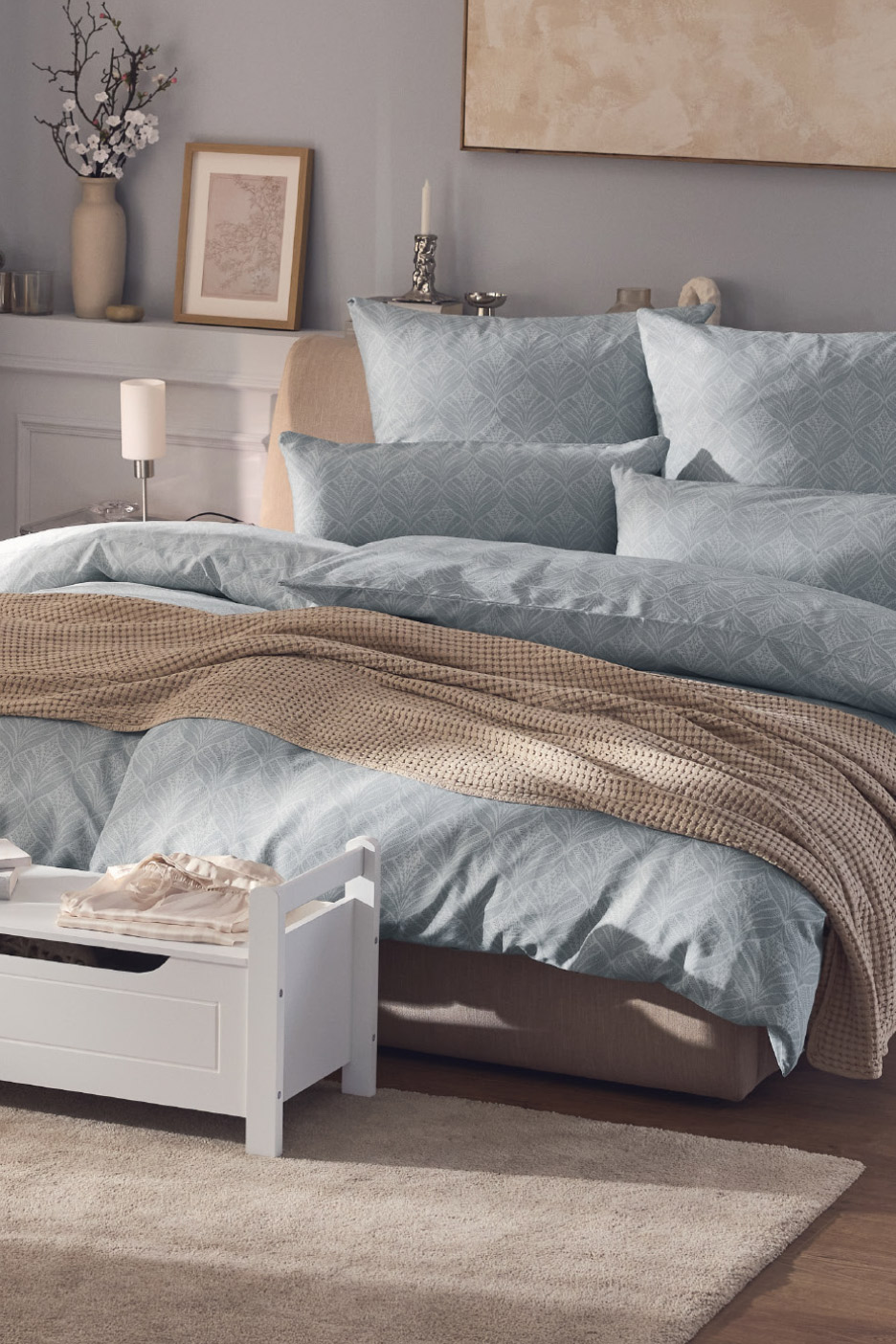 Bedroom with light blue patterned duvet cover, pillows, and a beige throw blanket.