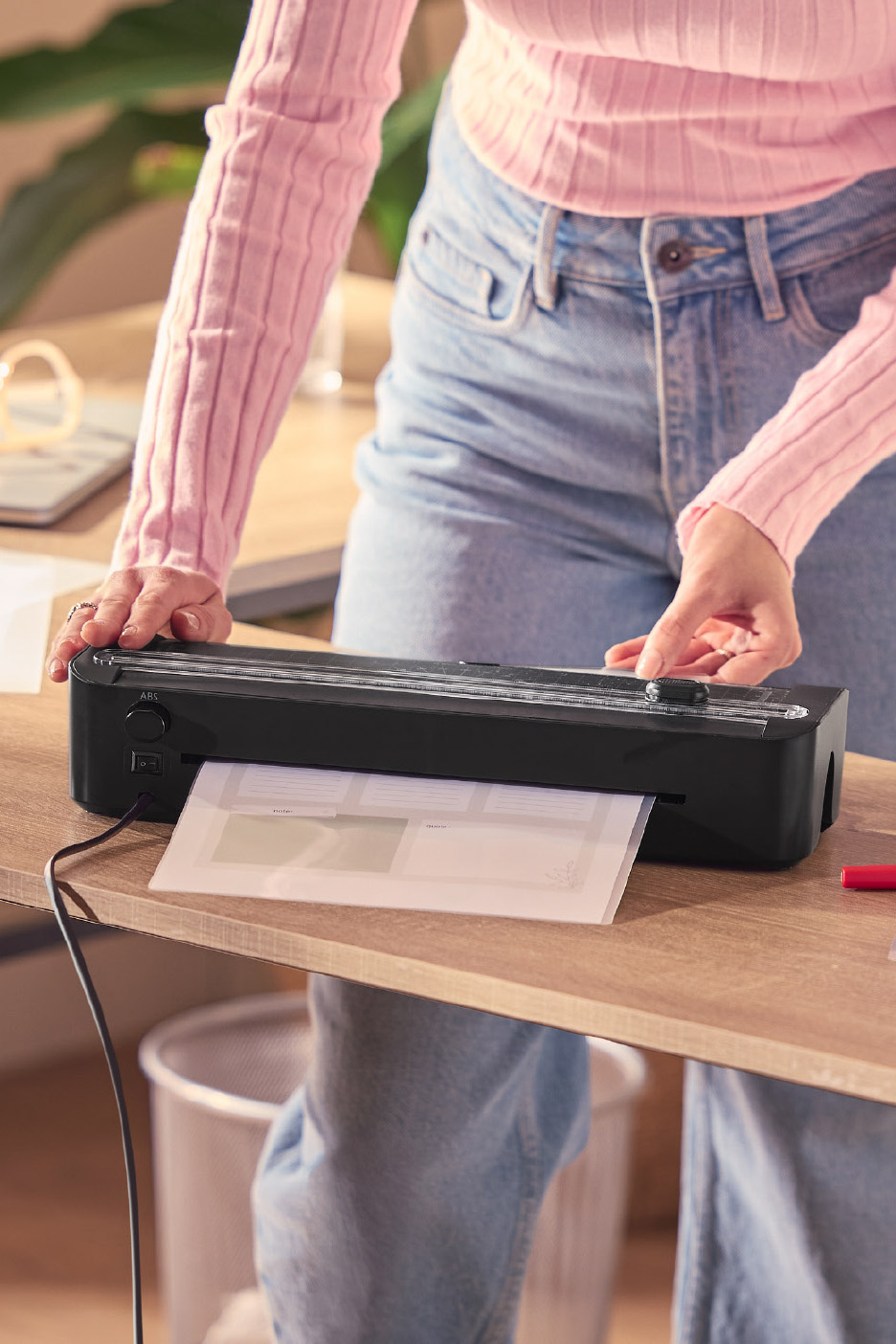 Person laminating documents with a black laminator on a wooden desk.