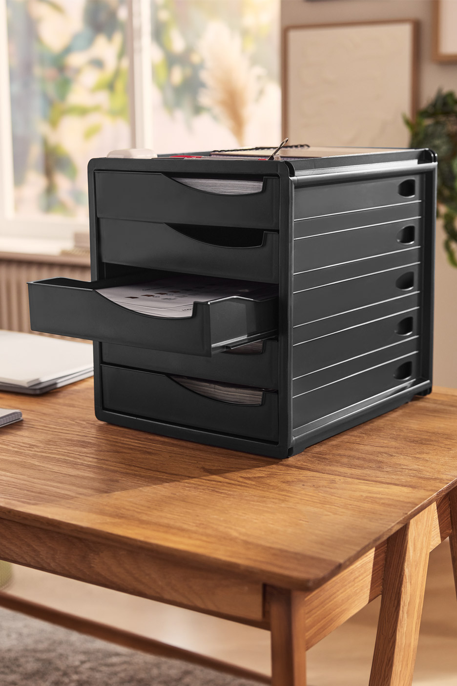 Black desk organizer with multiple drawers, one open, on a wooden desk.