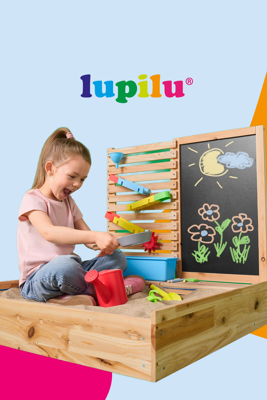 Happy girl playing in a wooden sandpit with a water wall and a chalkboard.