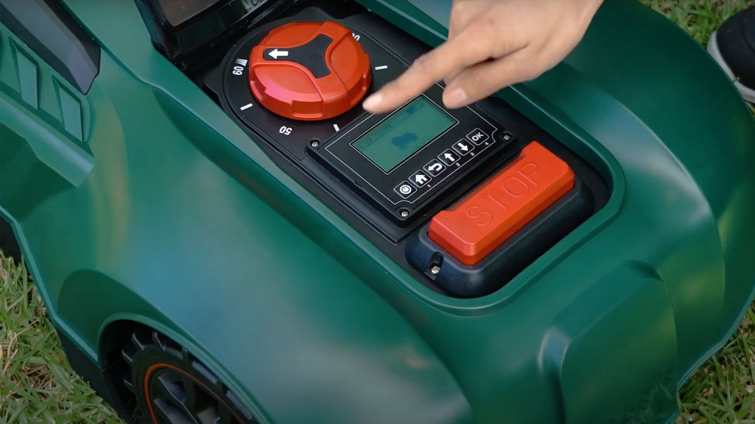 A person's hand operates the control panel of a Parkside robotic lawnmower.