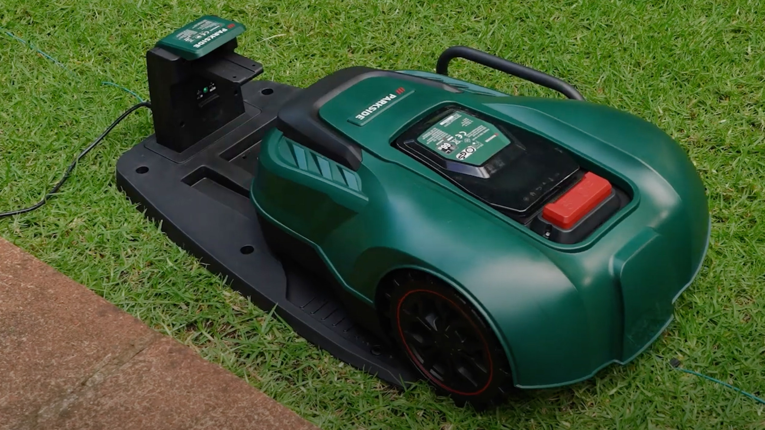 A Parkside robotic lawnmower is docked on its charging station in a lush green lawn.
