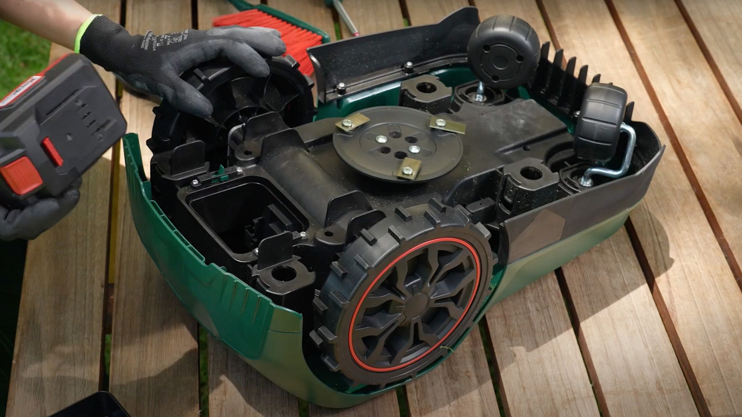 A person is repairing a robotic lawnmower, removing a battery and blade.