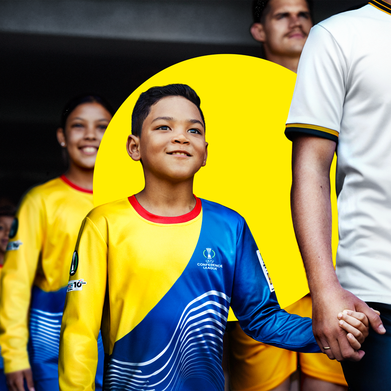 A young boy in a yellow and blue football jersey holds an adult's hand.