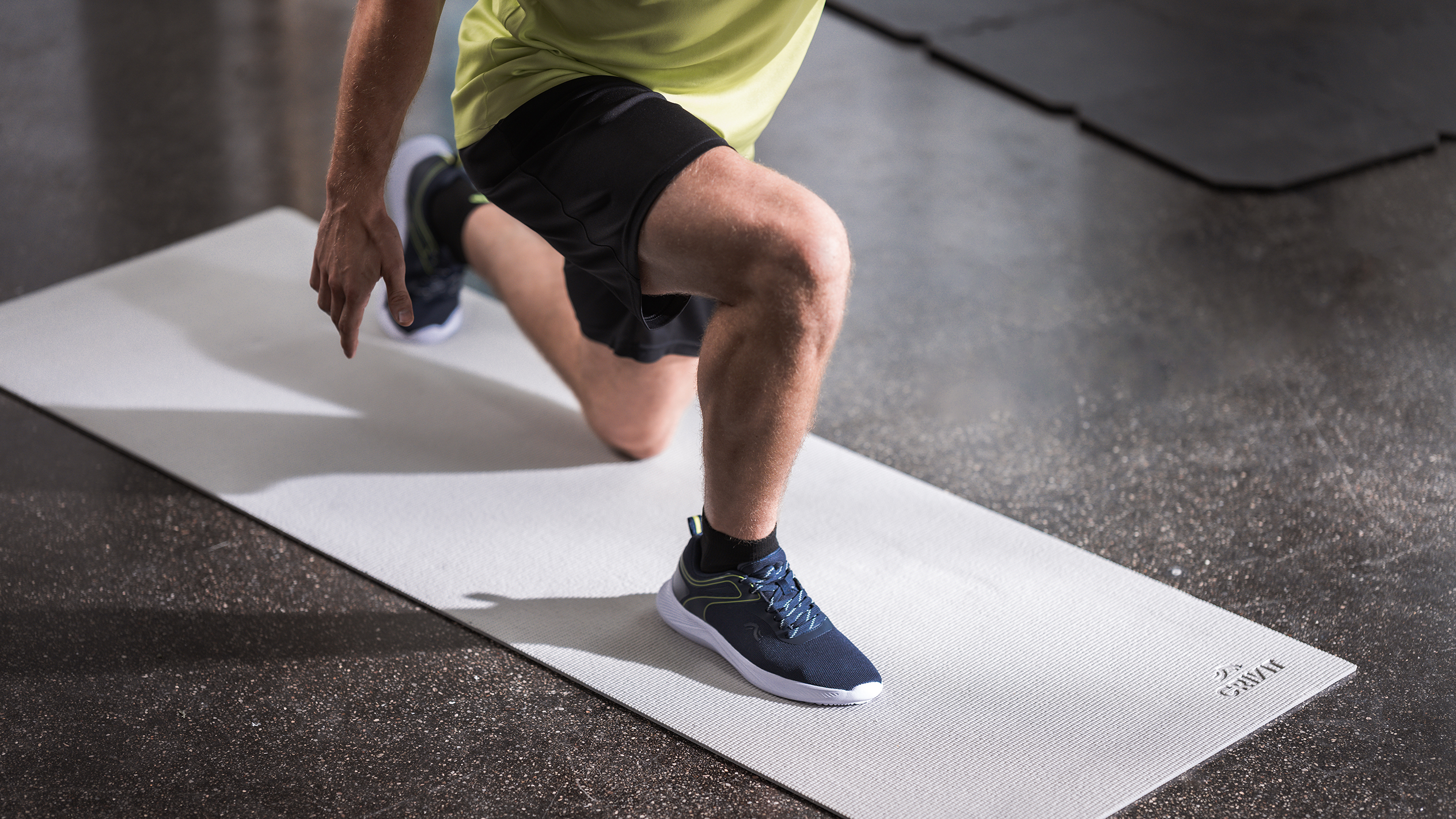 Man in athletic wear doing lunges on a light grey exercise mat.