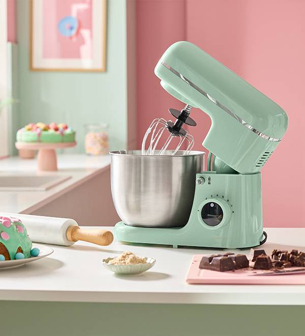 Mint green stand mixer with a stainless steel bowl on a kitchen counter with baking items.