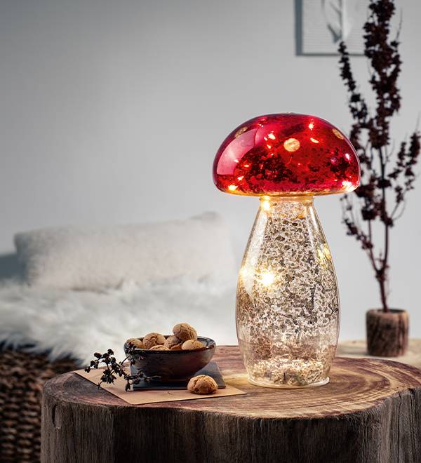 A red mushroom-shaped lamp with internal lights sits on a wooden table next to a bowl of cookies.