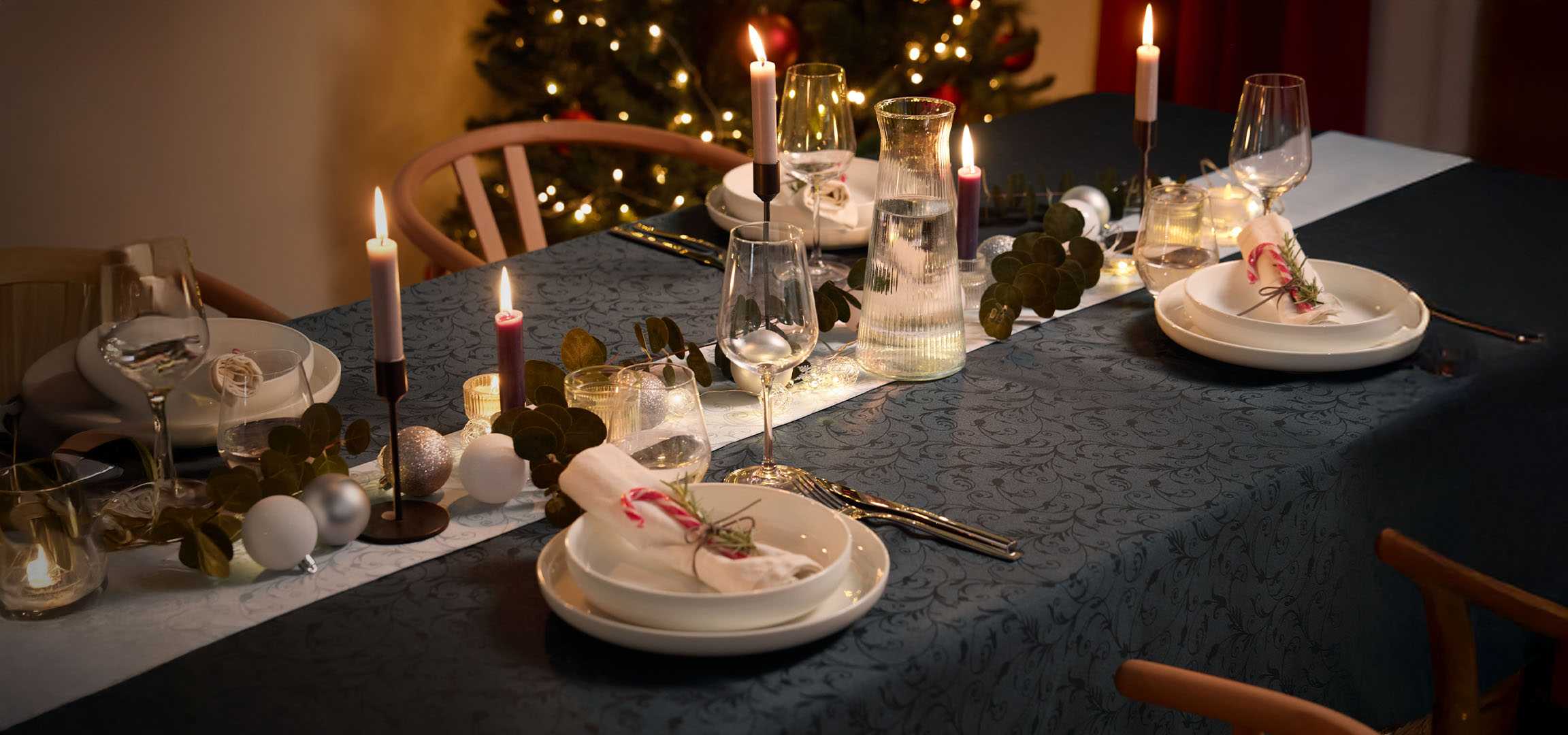 Christmas table with candles, white dinnerware, and festive decorations.