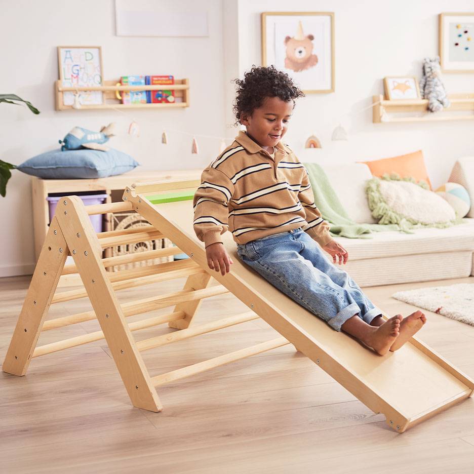 Child playing on a wooden slide and ladder in a child's room.