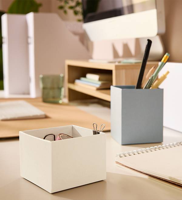 A tidy desk with a light gray pen holder, a white storage box, and a monitor stand.