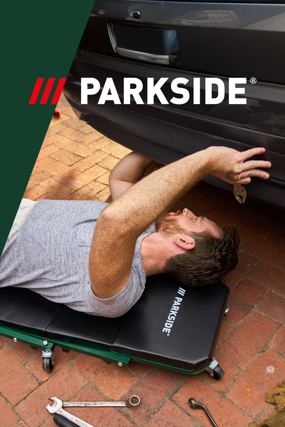 Man on a mechanic creeper working under a car, with tools on the ground.