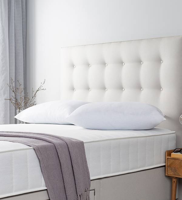 A white upholstered headboard and mattress set with a grey throw blanket.