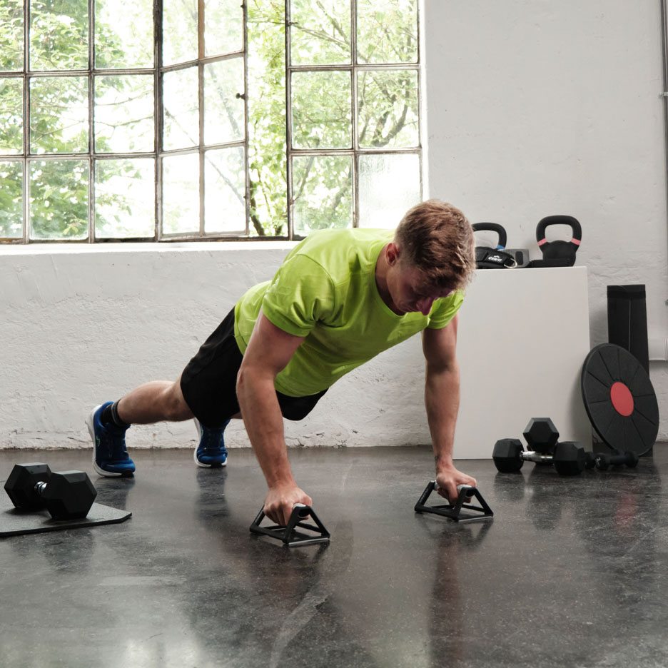 Man doing push-ups with push-up handles in a gym.