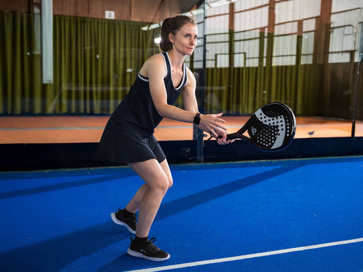 Woman in black padel dress with black padel racket on blue court.