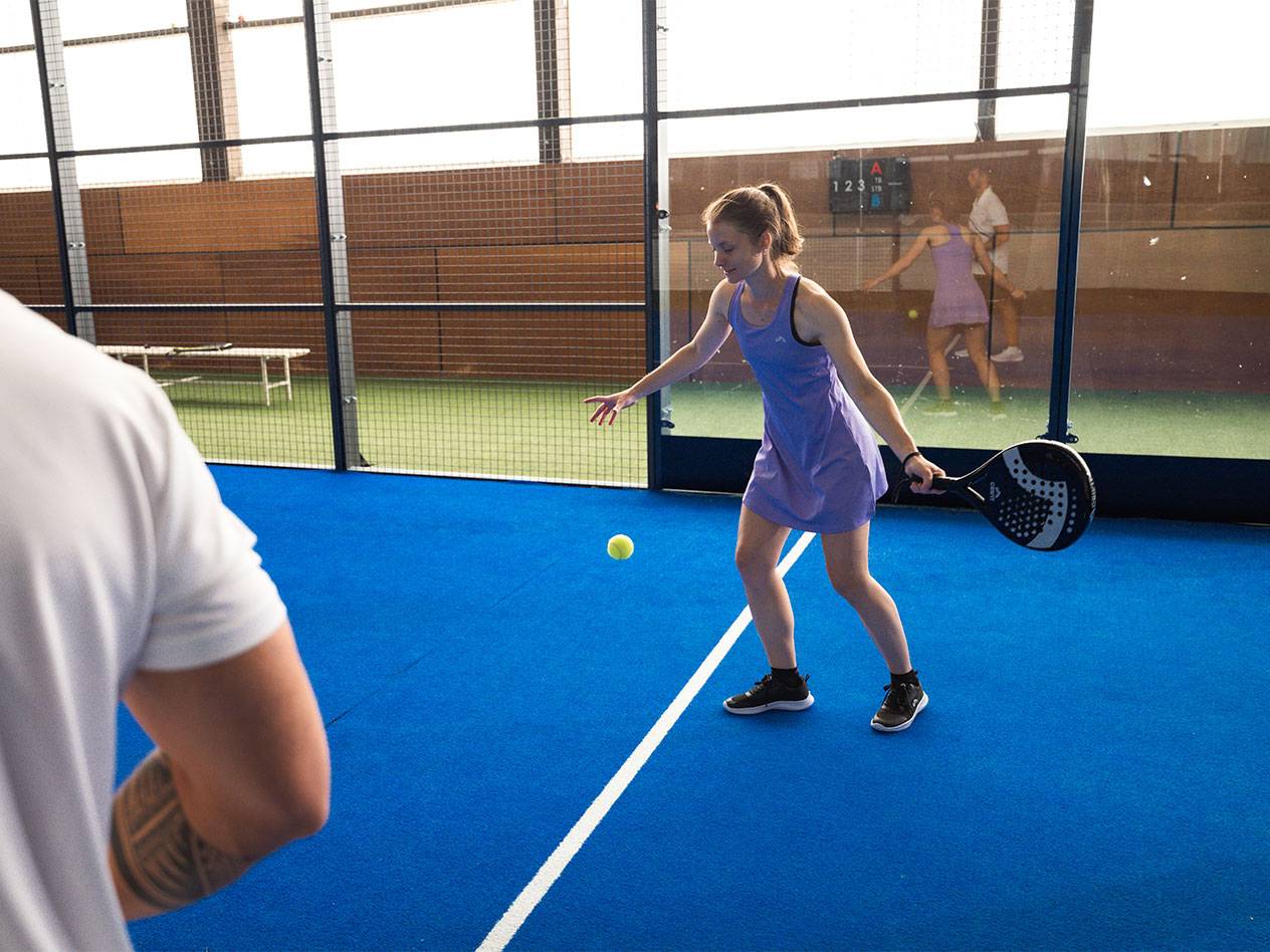 Woman in a purple sports dress playing padel with a racket and ball.