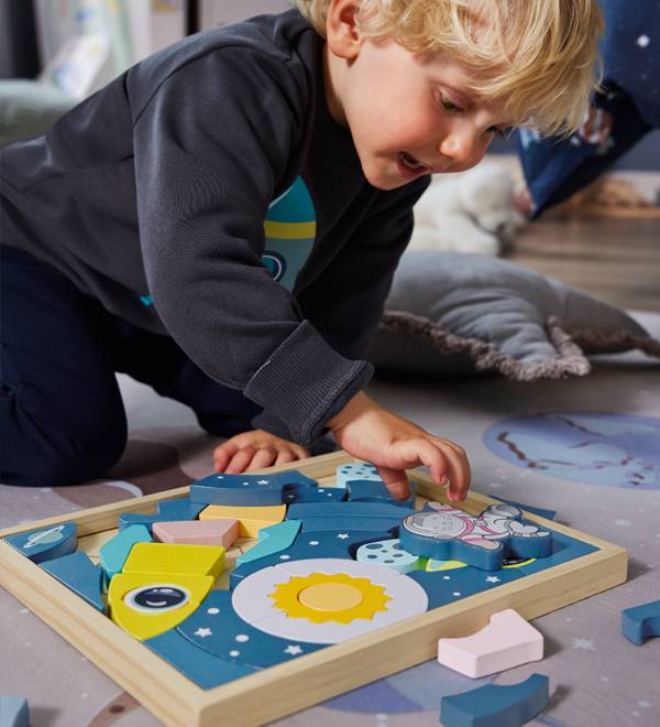A child playing with a space-themed wooden puzzle on a rug.